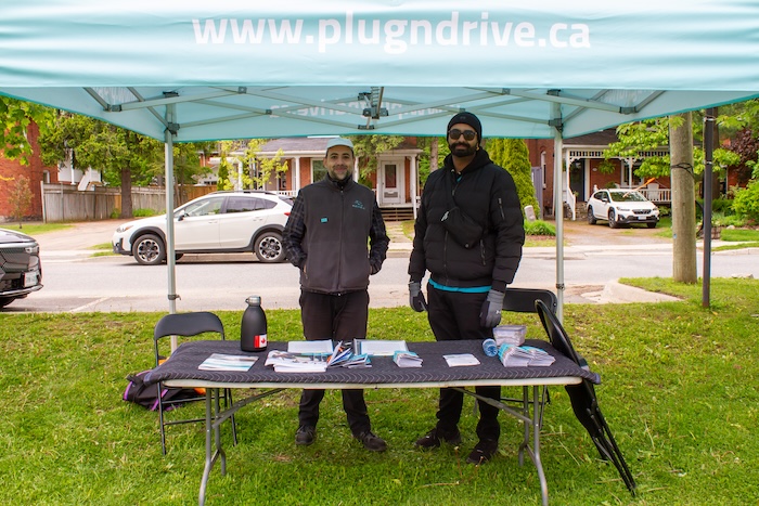 Two men standing under a Plug'n Drive pop up tent